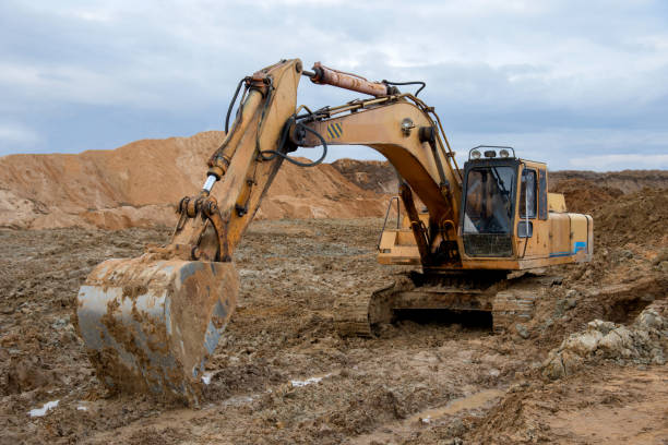 istock Excavator working at construction site. Backhoe digs ground for the foundation and for paving out sewer line. Construction machinery for excavating, loading, lifting and hauling of cargo on job sites 1257918685