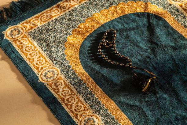 prayer beads and Noble Koran on Praying Carpet with Natural Light prayer beads and Holy Noble Quran Book with Calligraphy leather cover on a Decorated Praying Carpet with Natural Light rays floral crown photos stock pictures, royalty-free photos & images
