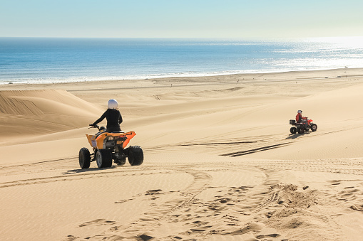 Two happy quad bikers driving in sand dunes. Young active couple in outdoor activity driving quad ATV on coastal desert beach, Africa, Namib desert, Namibia, Walvis Bay, Swakopmund.