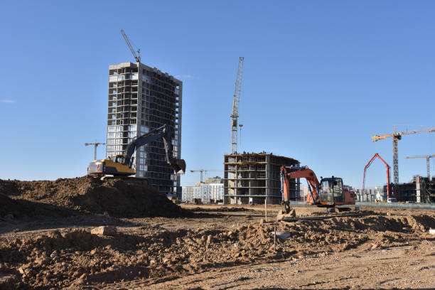 istock Excavators on earthworks. Backhoe on road work digs ground. Work of tower cranes at construction site Paving out sewer line. Construction machinery for excavating foundation, loading and lifting cargo 1257919637