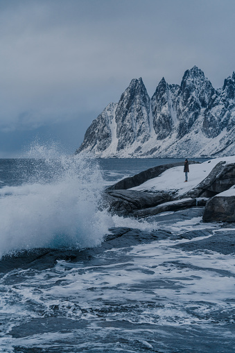 Woman looking at  seaside in winter  standing on rock near the storming sea on Lofoten island