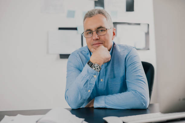 istock handsome gray-haired man sits in his office while working on business project looks satisfied, work routine concept 1257921316