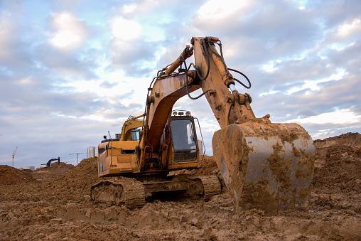 Excavator working at construction site. Backhoe digs ground for the foundation and for paving out sewer line. Construction machinery for excavating, loading, lifting and hauling of cargo on job sites