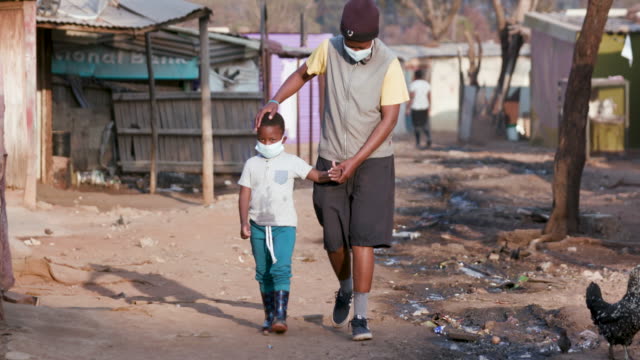 Black African mother and child walking in an informal settlement with protective face masks to prevent Covid-19