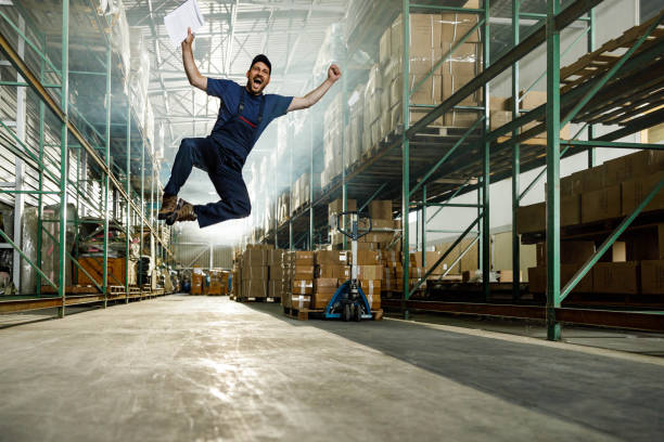 Cheerful manual worker jumping of joy in distribution warehouse.