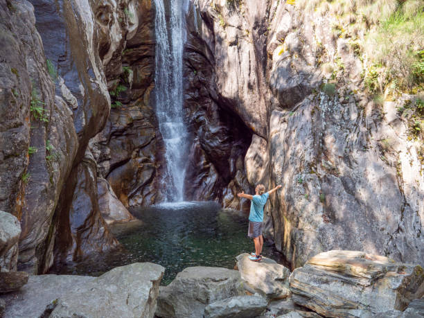 uomo si alza le braccia distese davanti alla cascata in svizzera - waterfall falling water maggia valley switzerland foto e immagini stock