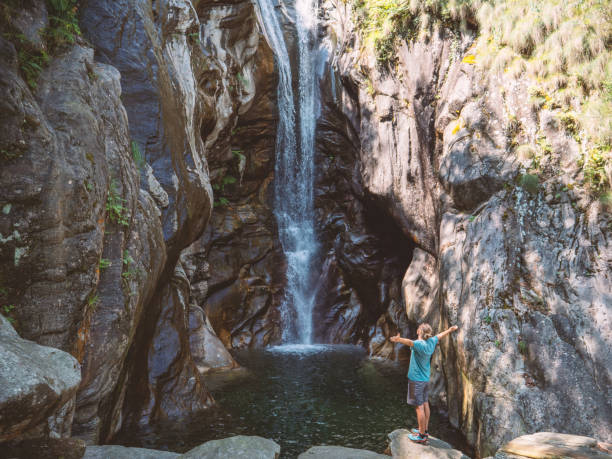 uomo si alza le braccia distese davanti alla cascata in svizzera - waterfall falling water maggia valley switzerland foto e immagini stock