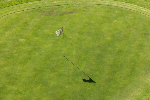 Aerial view of a golf course. In detail you can see the lawn of the hole and white flag of signaling. The sun shines and is an ideal day for sports and outdoor activities.