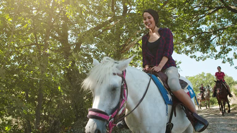 Four active people riding horses on a sunny outdoor wild forest field.Friends italian trip in Umbria.4k slow motion