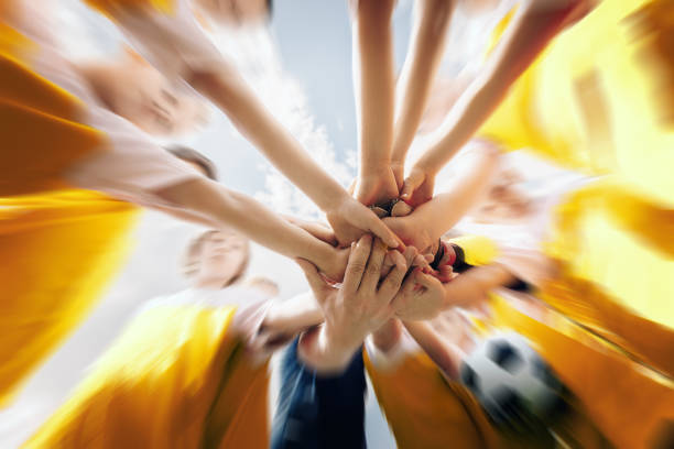 low-winkel-aufnahme einer gruppe von sportmannschaft bilden eine huddle mit ihren händen. sportteam stapelt händeseitfrei vor dem spiel. himmel mit wolken im hintergrund - mannschaftsfußball stock-fotos und bilder