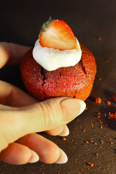 The girl's hand holds a chocolate cupcake decorated with a strawberry slice