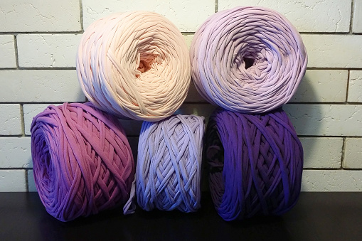 Vivid lilac, pink, violet, purple, balls of eco t-shirt yarn zpagetti for hand knitting are on wooden table with brick wall background. Recycled craft product.