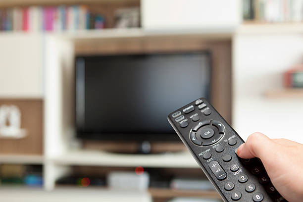 istock hand holding TV remote control toward television 125793904