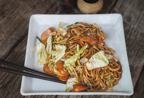 Yakisoba with sausage Japanese style fried noodle with sweet sauce in white plate with low sun lighting.