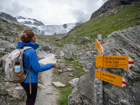 Woman with backpack hiking in Summer in Switzerland on overcast day looking at mountain map