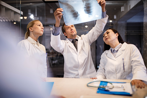 Group of doctors working in the office while two of them cooperating and analyzing medical scan.