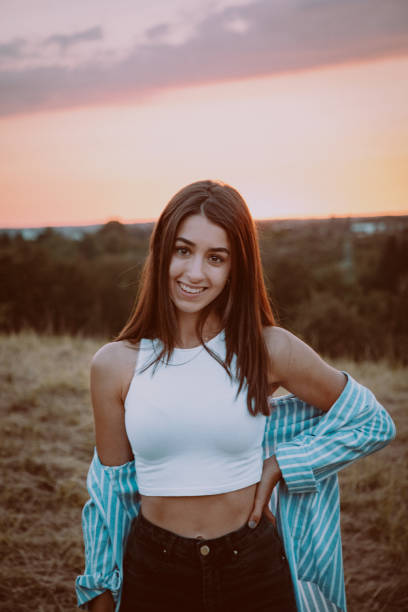 Summer Happiness. Smiling young teenage woman standing in summer field during sunset, looking over to the camera with a bright happy smile.. Young Millennial Generation Female Teenage Outdoor Lifestyle Portrait.