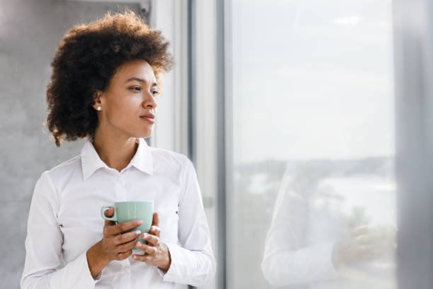 Pensive black woman looking through window during home isolation.