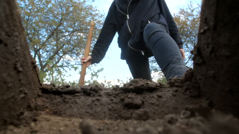 An unrecognizable person in dark clothes is digging a square pit against a blue sky with clouds. Point of view from the grave into which soil is sprinkled from a shovel.  Slow motion 50 fps 4k