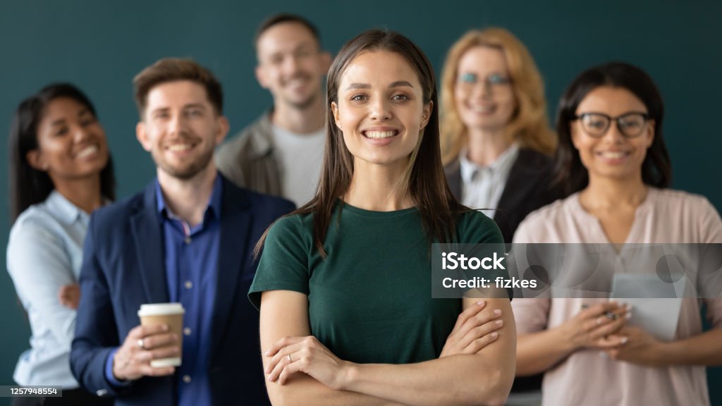 Close up headshot portrait of happy businesswoman hands crossed posture. Close up headshot portrait of happy businesswoman hands crossed posture. Different age and ethnicity businesspeople standing behind of female company chief business. Leader of multi-ethnic team concept Employee Stock Photo