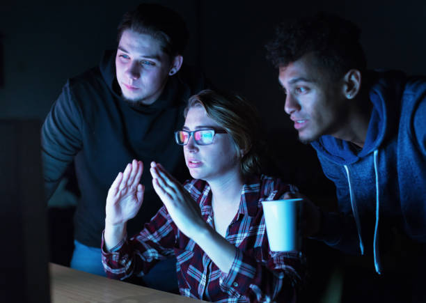 Group of young male and female tech workers collaborating as they interact with a computer at night