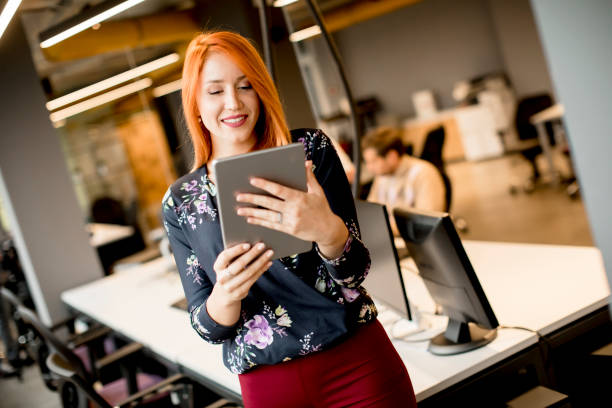 istock Young businesswoman working on digital tablet while in the background team working in the modern office 1257954238