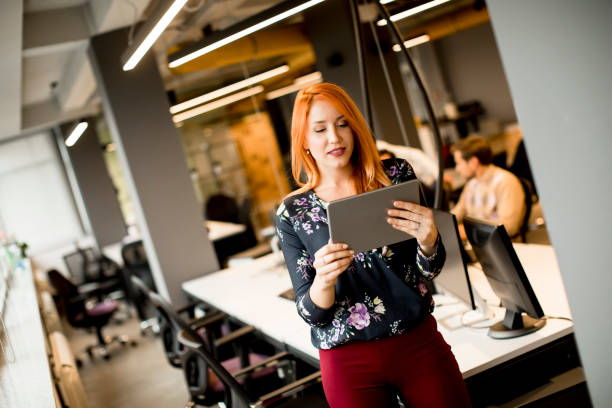 istock Young businesswoman working on digital tablet while in the background team working in the modern office 1257954246