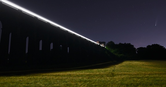 Long exposure image of Comet Neowise and the Ouse Valley Viaduct in Haywards Heath. Taken at night, the train can be seen crossing the bridge and the light from the train lights up the grass in the field.