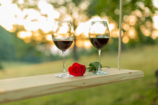 Two glasses of red wine and beautiful red rose lying on a swing