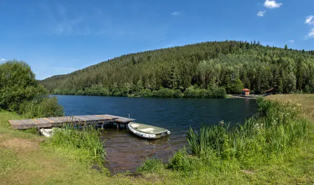 Jetty with boat on the upper lake of the dam Nagoldtalsperre near Seewald Erzgrube in the Black Forest, Germany - on the right the middle dike with bridge