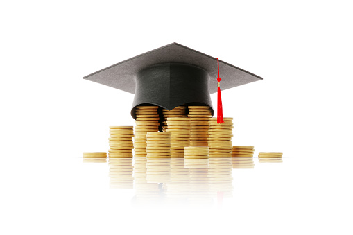 Black graduation cap sitting above coin stacks over white background. Horizontal composition with clipping path and copy space. Savings concept.