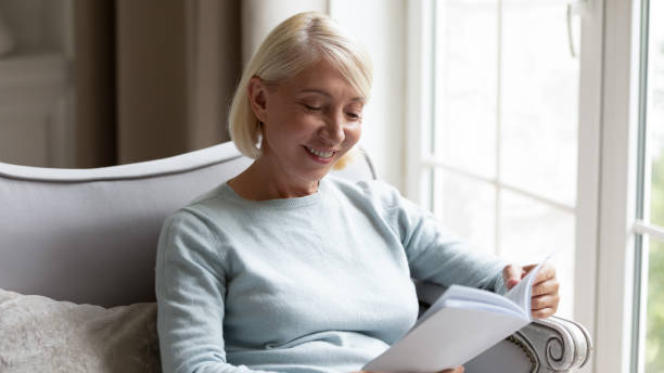 istock Happy elderly woman reading book relaxing at home 1257964321