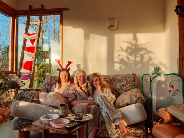 Multi-Generation Family on Christmas Day Two sisters are sitting on the sofa in the living room with their Grandmother on Christmas Day. They are wearing their pyjamas and costume reindeer antlers whilst smiling towards the camera. 12 17 months stock pictures, royalty-free photos & images