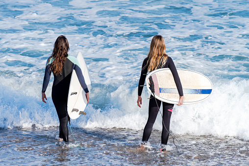 Two sporty surfing girlfriend with big longboard surf surfboard board. Modern active sport lifestyle and summer vacation. Long hair women.