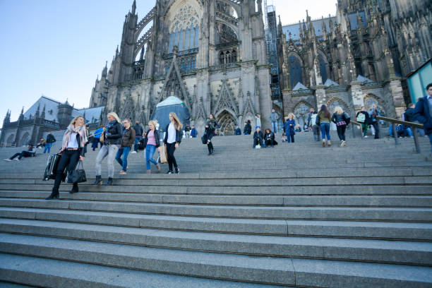 Many people on steps at Cologne cathedral in autumn. Steps are connecting squares Bahnhofsvorplatz and Domplatte. Most people are walking, other people are sitting and relaxing on steps