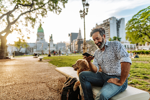 Mature Latino man with beard any stylish casual clothing in springtime day in Buenos Aires, Argentina walking his Retriever dog