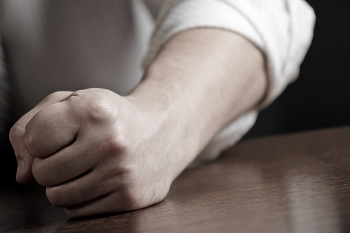 Close-up photo of a man hitting the desk with his clenched fist. Sepia toned. Shallow depth of field - focus on the fist. Space for copy. Can illustrate the concept of stress, disagreement, anger, etc.