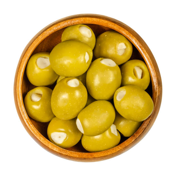 Big green olives stuffed with garlic cloves in wooden bowl Green olives stuffed with garlic cloves in wooden bowl. Big olives, fruits of Olea europaea, hand filled with pickled garlic pieces. Closeup from above, on white background, isolated macro food photo. olive tree cut out stock pictures, royalty-free photos & images