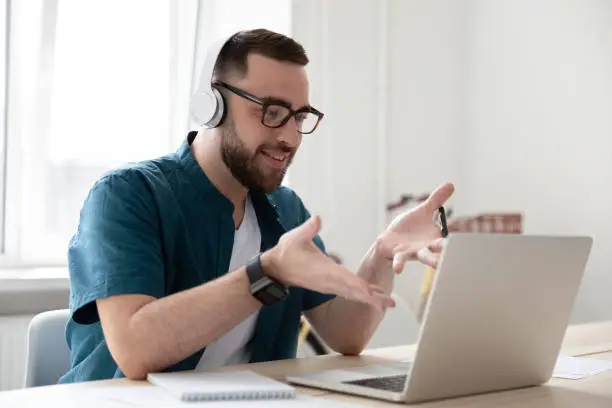 Photo of Smiling businessman in headphones looking at laptop screen watching webinar.