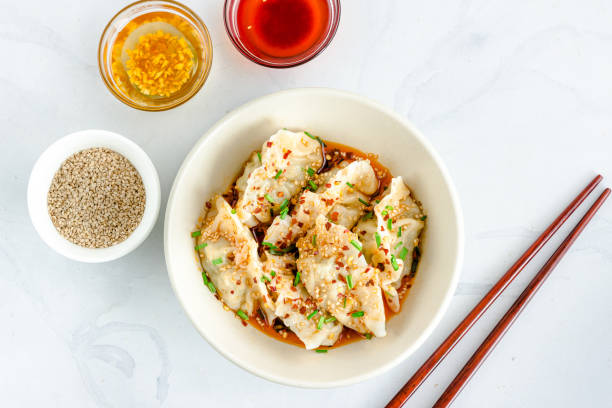 Spicy Sichuan / Schezwan Chicken Dumplings with Hot Red Chili Oil and Garlic Oil Top View Horizontal Photo Chicken Dumplings / Wonton in Spicy Sichuan Sauce in a Bowl with Chopsticks, Garlic Oil, Chili Oil, Sesame Seeds, Garlic Chives chicken dim sum stock pictures, royalty-free photos & images