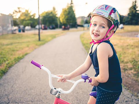 Young Caucasian girl on the bike outdoors. Exterior of public park.