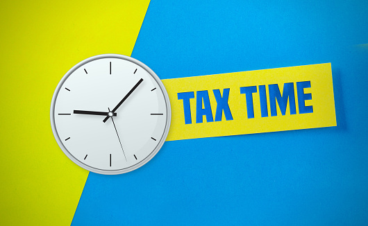 Clock and tax time message concept on colored yellow and blue paper. Horizontal composition with copy space.