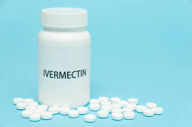 Photo of Treatments for Coronavirus (COVID-19): IVERMECTIN in white bottle packaging with scattered pills. Isolated on blue background. Horizontal shot. Copy space