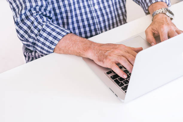 Senior man in plaid shirt typing on a gray laptop. Teleworking concept. stock photo