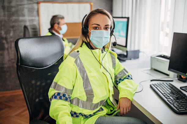 Young female police officer working in police office Young female police officer with protective face mask sitting in office and looking at camera. Senior male police officer working in background. civil servant stock pictures, royalty-free photos & images