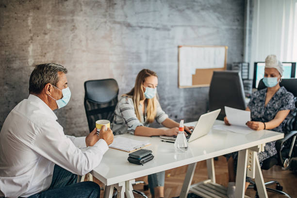 istock Mature man and two young woman working in office with protective masks 1257986078