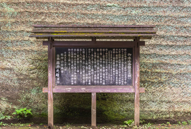 chiba, japan - july 18, 2020: Information panel in front of a stone quarry carved wall explaining the origins of the Nihonji temple of the buddhist St Zen sect on the slopes of the Mount Nokogiri.