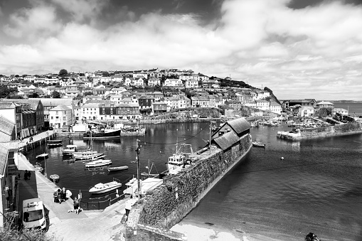 Mevagissey in Cornwall, England, UK.  This is a quaint Cornish fishing village with quintessential fishing harbour and fishing boats moored in the harbour.  Some tourists are on the harbour walls and piers.