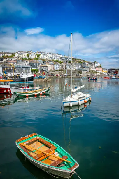 Mevagissey in Cornwall, England, UK.  This is a quaint Cornish fishing village with quintessential fishing harbour and fishing boats moored in the harbour.  Some tourists are on the harbour walls and piers. In the background a trawler is manoeuvring in the harbour to unload its catch.