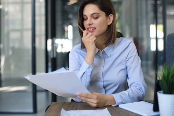 istock Attractive cheerful business woman checking paper documents in office. 1257997883